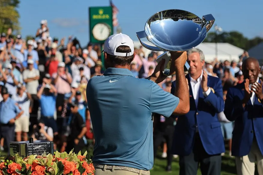 A polished golf trophy rests on a podium overlooking a scenic golf course fairway.